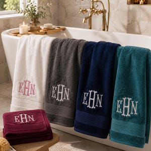 May include: A collection of five plush bath towels in white, charcoal gray, navy blue, teal, and deep burgundy. Each towel features a decorative embroidered monogram with the letters EHN in a classic script font centered on the lower section.