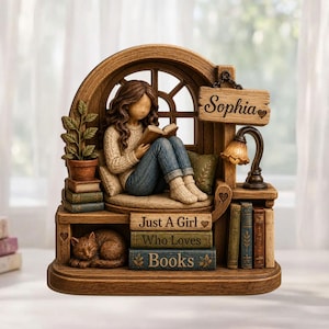 May include: A decorative figurine featuring a person with long brown hair reading a book while sitting in a wooden window nook. The piece includes a sleeping cat, a potted plant, a lamp, and books labeled "Sophia" and "Just A Girl Who Loves Books."