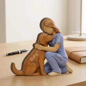 May include: A wooden figurine of a veterinarian hugging a brown dog. The dog's name, "Bailey," is inscribed on its side. The veterinarian is wearing blue scrubs with the name "Sophia" and a stethoscope. The figurine is on a wooden surface.
