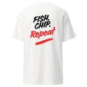 May include: White t-shirt with the text "FISH. CHIP. Repeat" in black and red. The design includes a red horizontal brushstroke under the word "Repeat". The shirt has short sleeves and a crew neck.