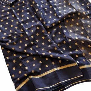 May include: Dark navy fabric with gold floral patterns and gold trim. The fabric is draped, showcasing the intricate design. The gold accents create a striking contrast against the dark background, highlighting the floral details.