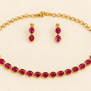 May include: A gold-toned necklace and matching pair of drop earrings, each featuring a series of oval-shaped, vibrant magenta-pink stones set in polished metal frames. The necklace consists of a linked chain with a lobster claw clasp.