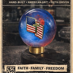 May include: A shift knob with a blue and red globe design featuring an American flag and cross. The knob has a brass base and is set against a vintage-style background with the text "CHAMBERLIN SPEED & CUSTOM".