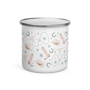 May include: White enamel mug with a silver rim, featuring a repeating pattern of cowboy boots, hats, horseshoes, stars, and steer skulls in muted colors of peach, blue, and gray. The mug is designed for beverages.