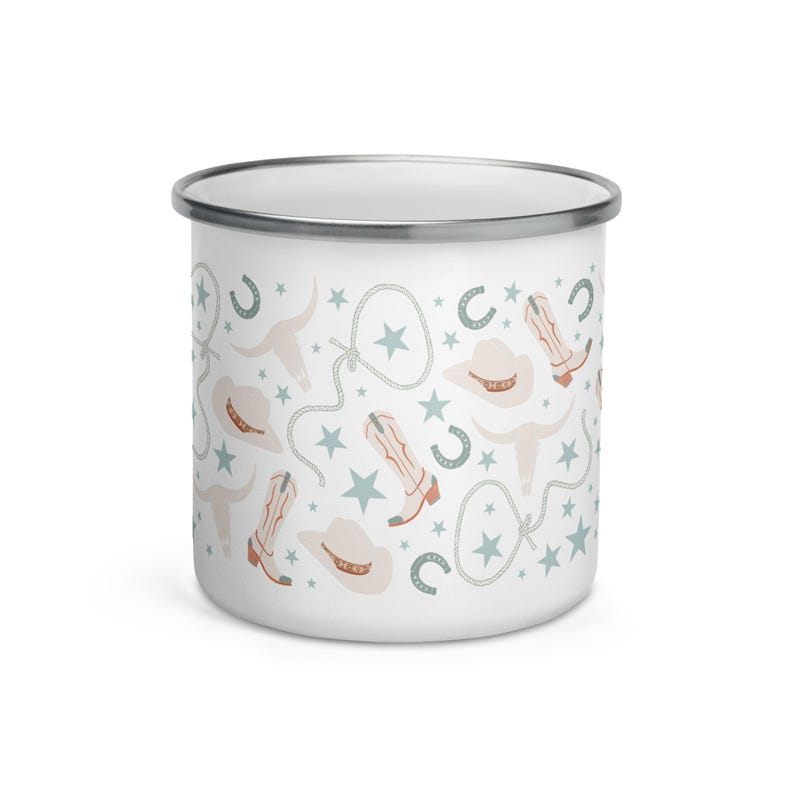 May include: White enamel mug with a silver rim, featuring a repeating pattern of cowboy boots, hats, horseshoes, stars, and steer skulls in muted colors of peach, blue, and gray. The mug is designed for beverages.