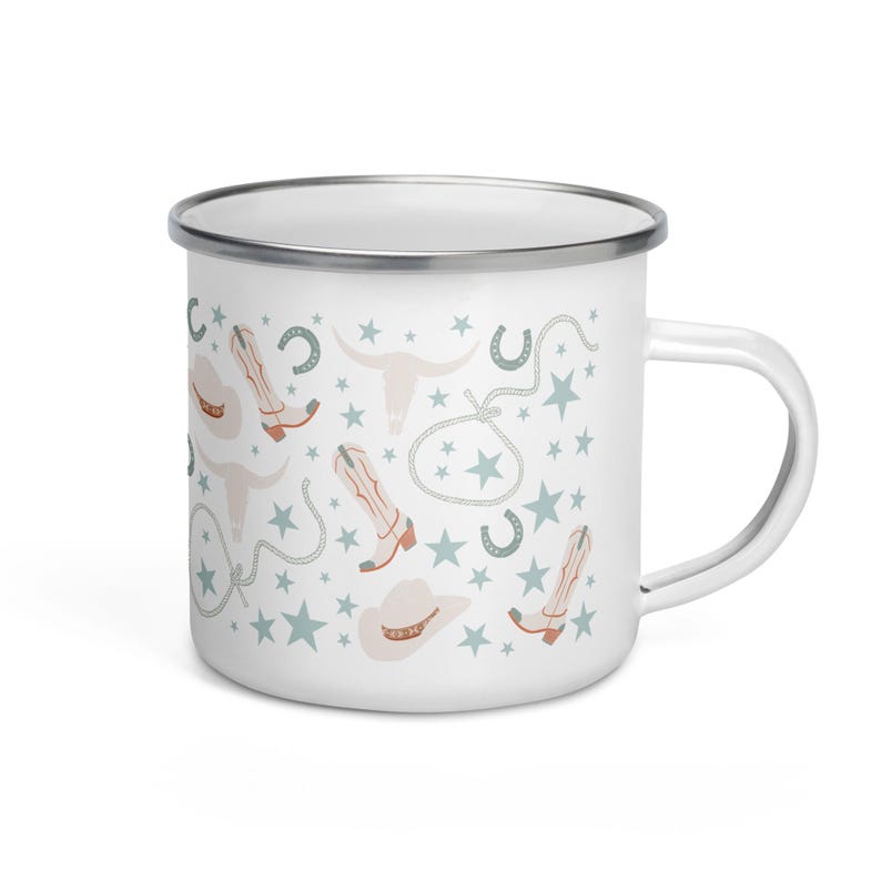 May include: White enamel mug with a silver rim and handle. The mug features a repeating pattern of cowboy boots, hats, stars, horseshoes, and longhorn skulls in muted colors. A charming and rustic design for a country-themed kitchen.