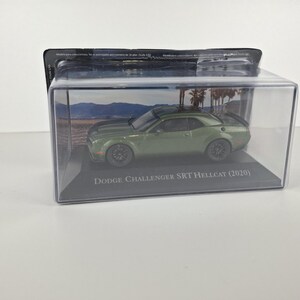 May include: A green Dodge Challenger SRT Hellcat (2020) model car displayed in a clear plastic case. The car has black wheels and is set against a backdrop of a beach scene. The text "Dodge Challenger SRT Hellcat (2020)" is printed on the base.