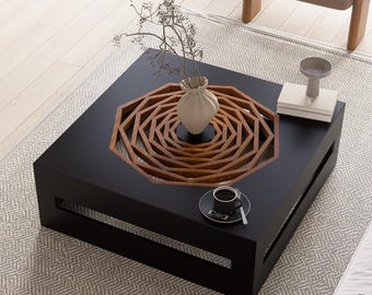 May include: An overhead shot of a modern living room with a black square coffee table featuring a wooden geometric design. A white sofa, chair, and rug are also visible. A cup of coffee sits on the table, and a vase with a plant is on top.