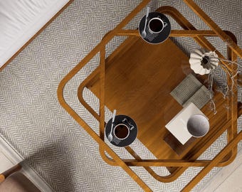 May include: Overhead view of a living room setup featuring a light brown wooden coffee table with two black saucers, each holding a cup of coffee and a spoon. A patterned rug and a white bed are also visible.