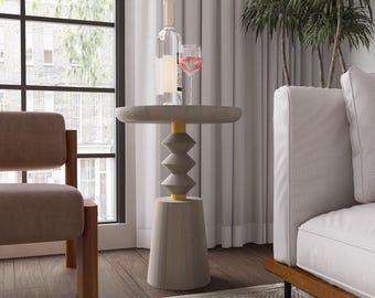 May include: A gray, modern side table with a round top and a geometric base. The table has a light gray finish with yellow accents. A bottle of wine and a glass of wine are on top of the table.