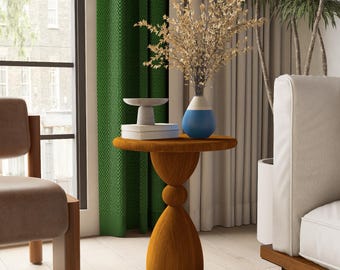 May include: A round, orange side table with a unique, hourglass-shaped base. The table has a small, circular top and is holding a white and blue vase with dried flowers. A small, white decorative piece and books are also on the table.