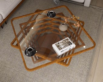 May include: A modern, geometric coffee table with a clear glass top and a wooden frame. The table features a unique, layered design with a square shape. Two black coffee cups with saucers are on the table, along with a book and a small vase.