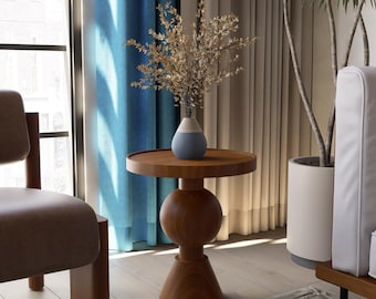 May include: A wooden side table with a round top and a spherical midsection. A vase with a blue and white design holds dried flowers. The table is set in a room with blue curtains and a neutral-toned rug.
