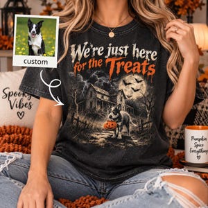 May include: A charcoal gray t-shirt featuring a graphic of a dog holding a pumpkin bucket in front of a haunted house under a full moon. The text reads We're just here for the Treats. An inset photo shows a black and white dog in a field.