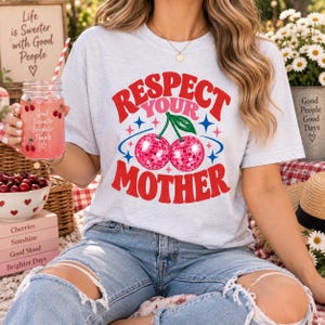 Op de afbeelding: Een lichtgrijs t-shirt met korte mouwen en een grafische print met de tekst RESPECT YOUR MOTHER in rode en roze letters. Het ontwerp bevat twee roze discobal-kersen met groene steeltjes, omringd door kleine blauwe en rode sterpictogrammen.