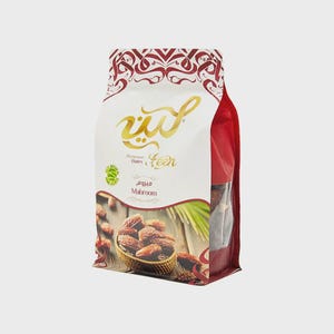 May include: A white and red food pouch containing Mabroom dates. The packaging features gold Arabic calligraphy, the text 'Premium Dates Leen', and 'Mabroom'. A graphic shows dates in a woven basket on a wooden surface with a green palm leaf.