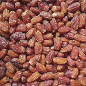 May include: A large collection of dried dates, each featuring a wrinkled, oval-shaped skin in varying shades of deep reddish-brown and amber. The fruits are packed closely together, displaying their natural, fibrous, and slightly glossy texture.