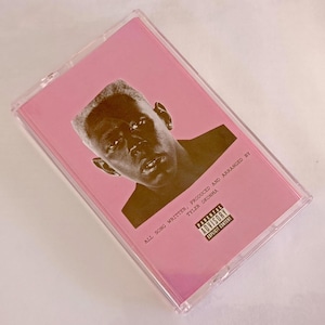Puede incluir: Un casete rosa con un retrato de una persona en la portada. El texto en la portada dice "ALL SONG WRITTEN, PRODUCED AND ARRANGED BY TYLER OKONMA" e incluye una advertencia para padres.