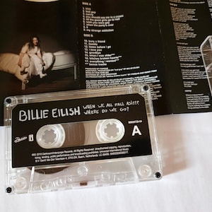 Op de afbeelding: Een transparante cassette met het album "WHEN WE ALL FALL ASLEEP, WHERE DO WE GO?" van Billie Eilish. De cassette zit in de hoes, met de albumhoes zichtbaar. De albumhoes toont een foto van Billie Eilish.
