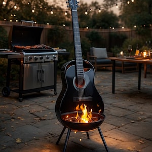 May include: A black guitar-shaped fire pit with a burning fire inside, set on a patio. A stainless steel grill is in the background, along with a table and chairs. String lights are strung overhead.