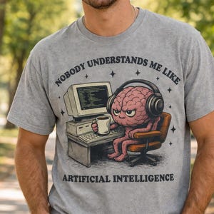 May include: Grey t-shirt featuring a cartoon brain wearing headphones, seated at a computer, and holding a mug. The text on the shirt reads "NOBODY UNDERSTANDS ME LIKE ARTIFICIAL INTELLIGENCE."
