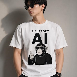 May include: White t-shirt featuring the text "I SUPPORT AI" in black. Below the text is a graphic of a chimpanzee wearing sunglasses and giving a thumbs up. The t-shirt has short sleeves.