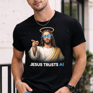 May include: Black t-shirt featuring an image of Jesus wearing blue sunglasses and a halo, pointing his finger. The text "JESUS TRUSTS AI" is printed below the image. The shirt is worn by a person in blue jeans.