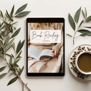 Puede incluir: Una tableta digital que muestra un diario de lectura, con el texto "Book Reading Journal". La tableta está rodeada por una taza de café, granos de café y ramas verdes, creando una escena acogedora.