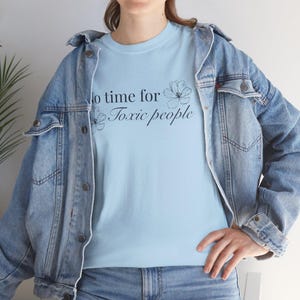 Puede incluir: Camiseta azul claro con la frase "No time for Toxic people" en escritura negra y detalles florales. Esta prenda informal está hecha de un tejido suave.