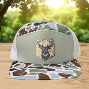 Może przedstawiać: Czapka typu trucker z wzorem kamuflażu z białym tyłem z siatki i płaskim daszkiem. Przedni panel jest beżowy z emblematem głowy jelenia wewnątrz sześciokąta. Daszek czapki ma brązowy, zielony i beżowy wz&oacute;r kamuflażu.