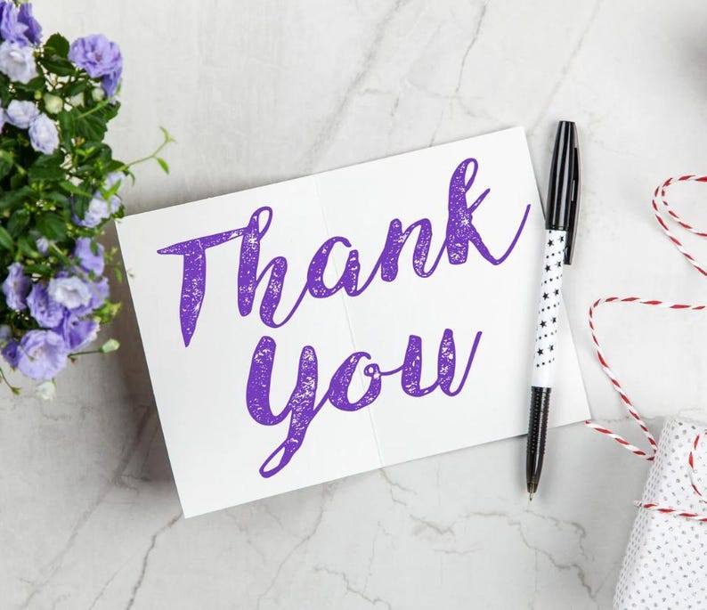 Może przedstawiać: Biała karta z fioletowym napisem "Thank You". Obok karty leży czarno-biały długopis z gwiazdkami. Obecny jest r&oacute;wnież mały prezent owinięty w biały papier z czerwoną i białą sznurkiem.
