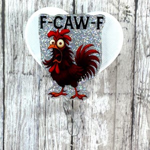 May include: A badge reel with a cartoon rooster design. The rooster is red and black with wide eyes and a surprised expression. The text "F-CAW-F" is above the rooster on a glittery background, attached to a white heart-shaped backing.