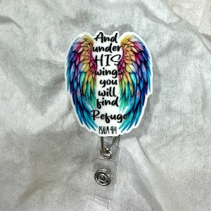May include: A badge reel with a colorful wing design and the text "And under HIS wings you will find Refuge" and "PSALM 91:4". The wings feature shades of blue, green, yellow, orange, and purple.