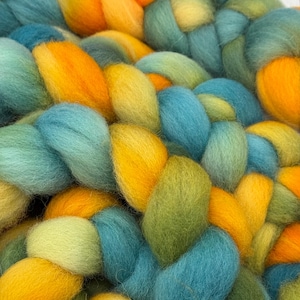 May include: A close-up of a hand-spun yarn with a blend of teal, yellow, and green colors. The yarn is arranged in a braided pattern.