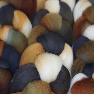 May include: A braided bundle of yarn in shades of brown, green, black, and white. The yarn is arranged in a pattern of alternating colors.