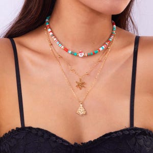 May include: A layered necklace featuring a festive Christmas theme. The top layer has a beaded design with red, white, and green beads, and a Santa Claus charm. The lower layers have gold-colored chains with a snowflake and Christmas tree pendant.