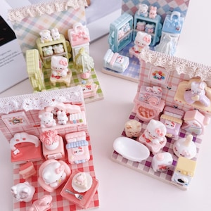 May include: Miniature dioramas featuring Hello Kitty and other characters in various settings. Each diorama includes furniture and accessories, with a checkered background and lace trim. The color palette includes pink, blue, and green.