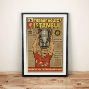 May include: Framed poster featuring a comic book style illustration of a soccer player holding a trophy above his head. The poster has the text "The Miracle of Istanbul" and "Liverpool win the Champions League". The color scheme is red, beige, and black.
