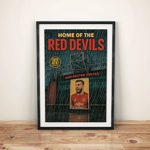 May include: Framed poster featuring a vintage-style illustration of Manchester United's stadium. The text "HOME OF THE RED DEVILS" is displayed above the stadium image. A portrait of a player in a red jersey is also included.
