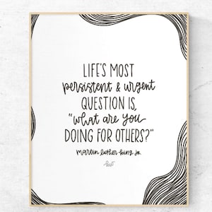 Puede incluir: Una impresión enmarcada con fondo blanco y texto negro. La cita dice: "LA PREGUNTA MÁS persistente y urgente DE LA VIDA ES: '¿qué estás HACIENDO POR LOS DEMÁS?'" de Martin Luther King Jr. Líneas onduladas negras enmarcan las esquinas superior e inferior.