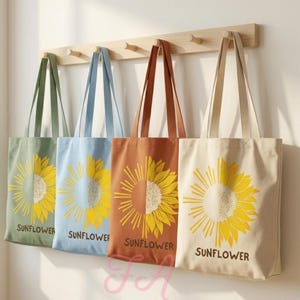May include: Four canvas tote bags hanging on a wooden rack. Each bag features a graphic of a sunflower split into two halves, one side colored and one side yellow, with the word SUNFLOWER printed in black at the bottom of each bag.