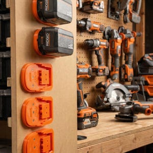 May include: A wooden panel displays several black and orange power tool batteries and charging bases. The batteries are labeled "RIDGID". Other power tools are visible in the background, including drills, saws, and grinders, all in matching black and orange.