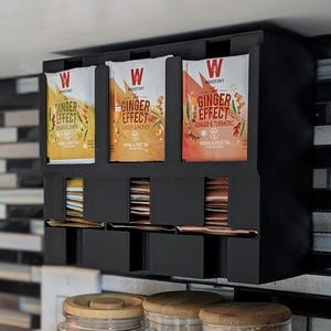 May include: A black wooden tea bag organiser with three sections, each holding a different flavour of "Ginger Effect" tea. The tea flavours are Ginger & Lemon, Ginger & Honey, and Ginger & Turmeric. Below are three glass jars with wooden lids.