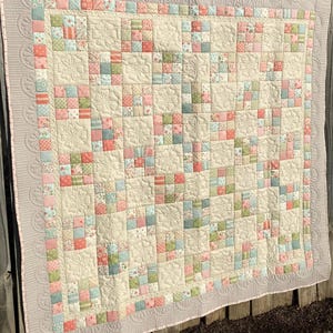 May include: A patchwork quilt featuring a grid of alternating cream-colored squares with embossed floral patterns and smaller multi-colored squares in shades of pink, green, and blue. The quilt has a wide, textured border with a scalloped design.