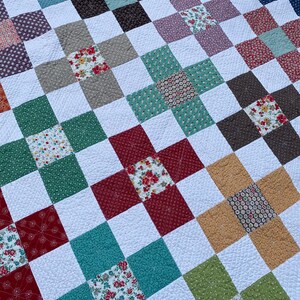 K&ouml;nnte beinhalten: Ein Patchwork-Quilt mit einem sich wiederholenden Gittermuster aus wei&szlig;en Quadraten, die mit bunten Quadraten durchsetzt sind. Die farbigen Quadrate zeigen verschiedene Blumenmuster, einfarbige Texturen sowie geometrische Muster in Rot, Gr&uuml;n, Blau und Gelb.