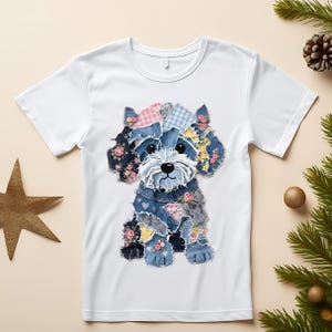 May include: White t-shirt featuring a whimsical patchwork dog design. The dog is composed of denim patches adorned with floral patterns and pink gingham. The dog's face is white with black accents, and it sits centered on the shirt.