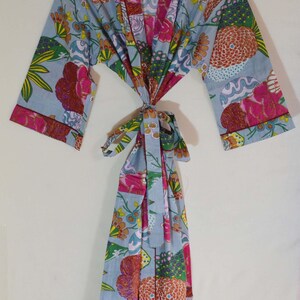 May include: A light blue floral print robe with a tie closure. The robe features a colorful pattern of flowers in shades of pink, orange, green, and yellow. The sleeves and edges are trimmed with a pink border.