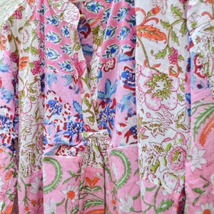 May include: A collection of floral print shirts in pink, white, blue, and green. The shirts are hanging on a wooden hanger. The fabric features a patchwork design with various floral patterns, creating a vibrant and colorful aesthetic.