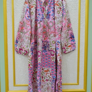 Peut inclure: Une robe midi à manches longues présentant un motif patchwork avec divers imprimés floraux et botaniques dans des tons de rose, blanc, bleu et vert. La robe possède un col mao, une patte de boutonnage avant et des fentes latérales à l'ourlet.