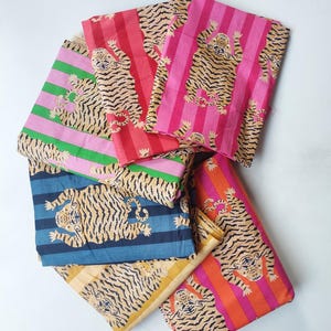 Puede incluir: Un conjunto de telas coloridas con estampado de tigre. Las telas presentan un patrón repetido de tigres con rayas negras sobre un fondo beige, combinados con rayas verticales en varios colores, incluyendo rosa, rojo y azul.